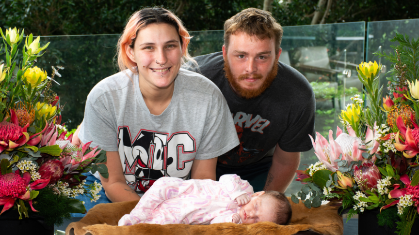 Family photo of mother, father and baby. Surrounded by native flowers.